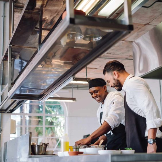 Two cooks preparing food in restaurant kitchen Happy male chefs cooking food at cafe kitchen and talking. Two cooks preparing food in restaurant kitchen.