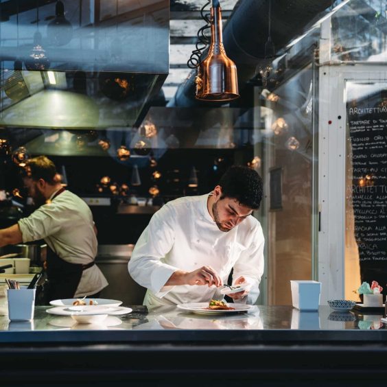 A chef is cooking in his restaurant’s kitchen A chef is cooking in his restaurant's kitchen. Shot through the glass. High-end gourmet restaurant.